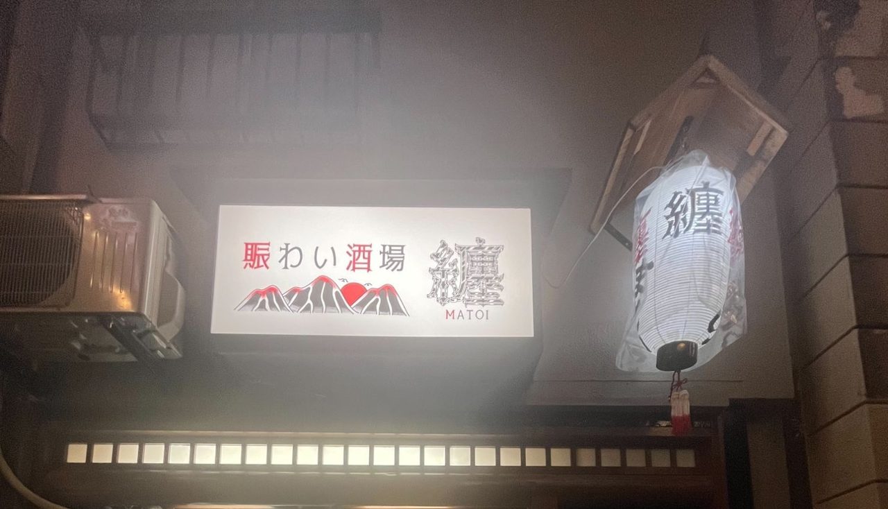 夜の外観。光る「賑わい酒場 纏」の看板と白い提灯