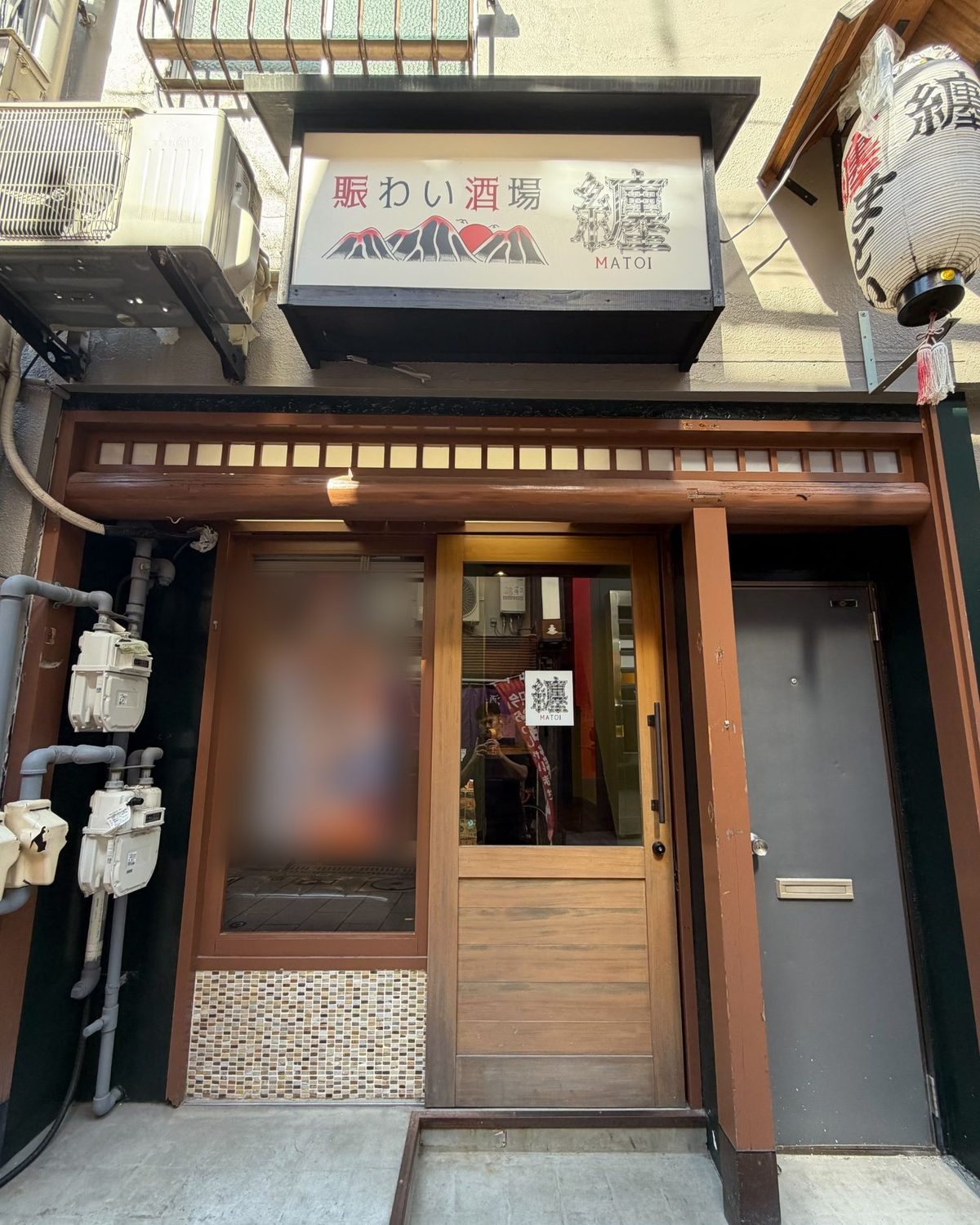 昼の外観。「賑わい酒場 纏」の看板と提灯、木の扉